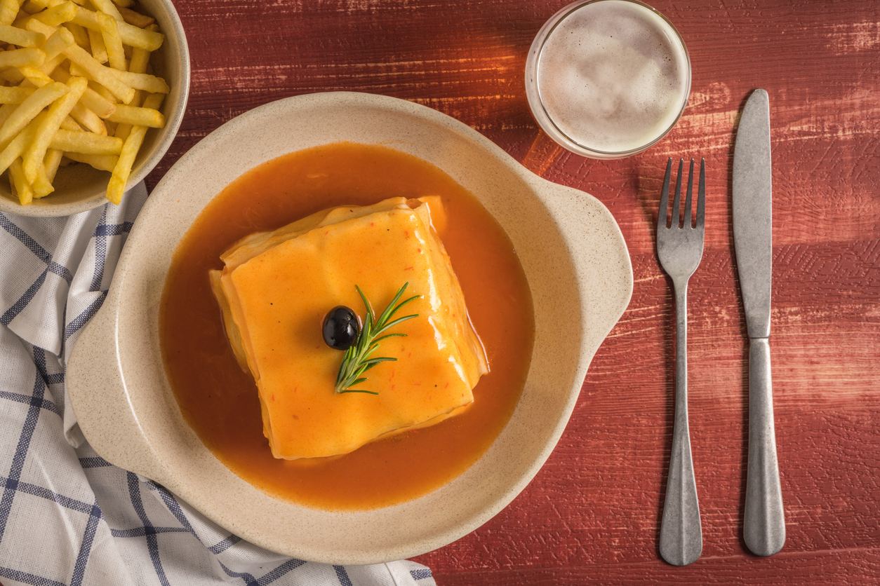 Francesinha sandwich covered in melted cheese and sauce, topped with an olive