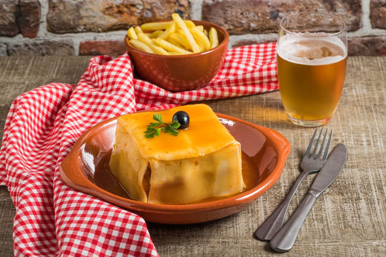 Francesinha served in a clay dish with a basket of fries beside it