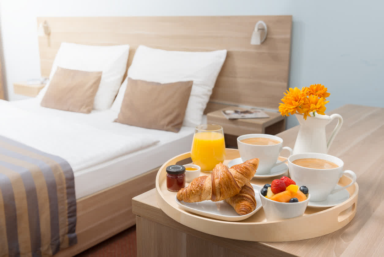 Breakfast tray with croissants, coffee and fruit beside the bed