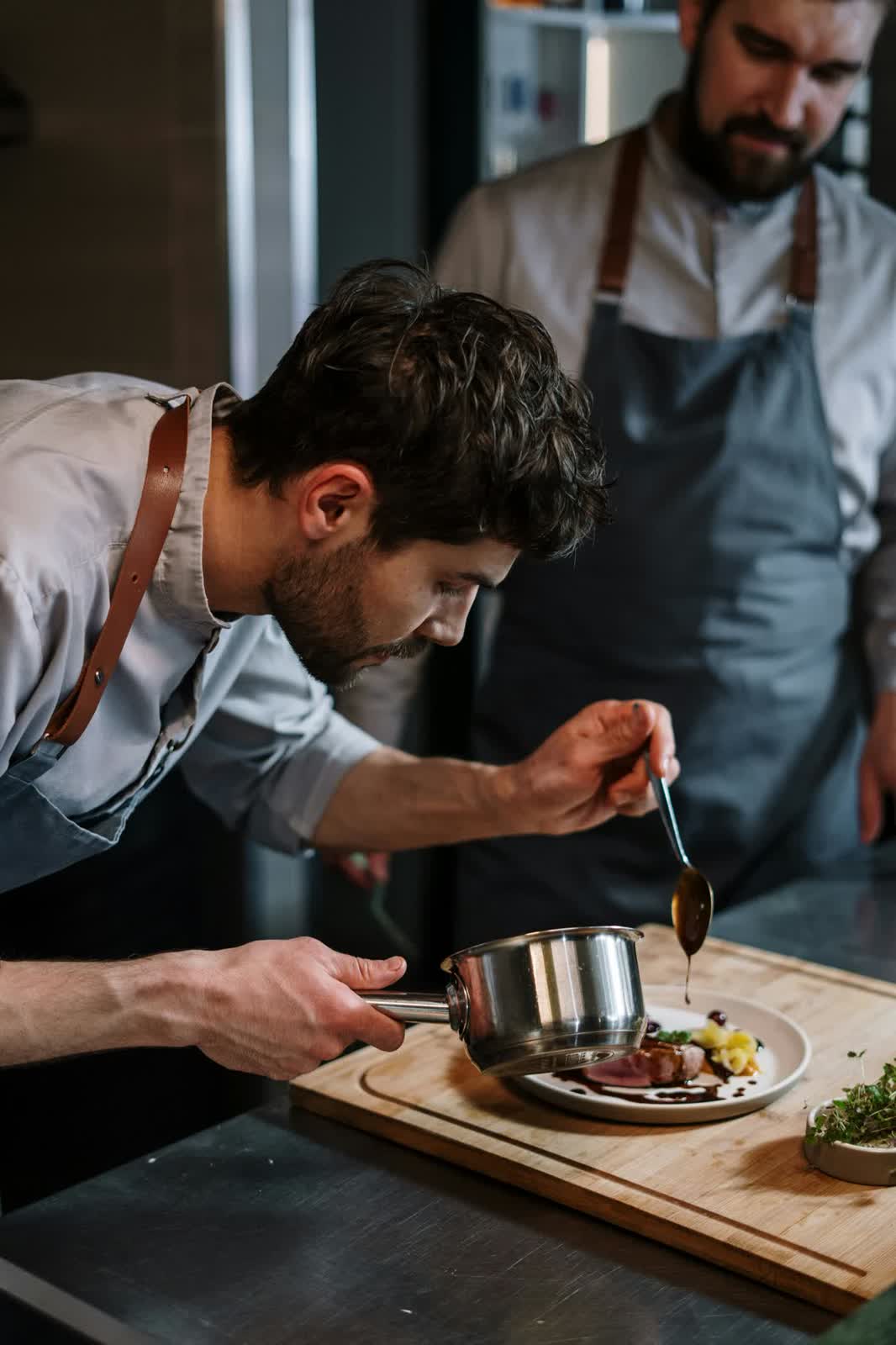 Chef spooning sauce over a plated dish in the kitchen